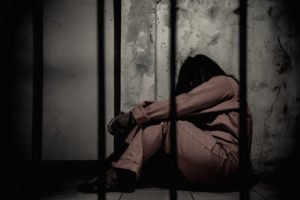 A woman in an orange jumpsuit behind prison bars.