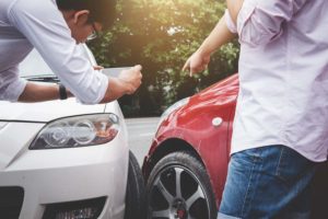 A young man on a phone looks at a car accident.