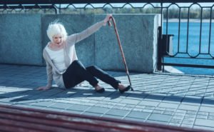 An older woman tries to get up after a fall on a sidewalk.