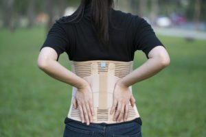 A woman in a back brace holds her back in pain.