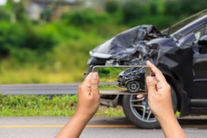 person taking a picture of the damaged front-end of a car