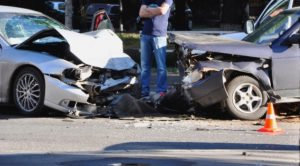 guy standing between two smashed-up cars