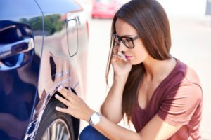 woman calls insurance while inspecting vehicle damage